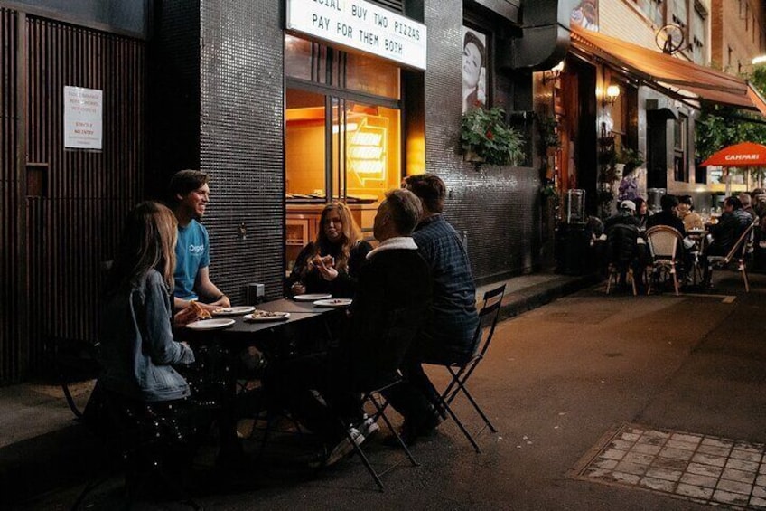 An outdoor café with tables and chairs, a sign above the entrance, and a street with other establishments in the background. 4