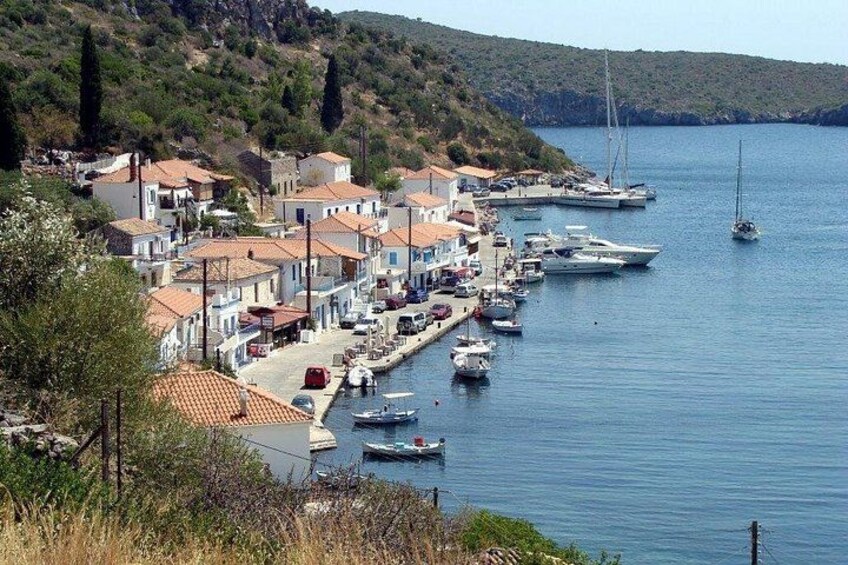 A coastal village with terracotta-roofed buildings, a marina with sailboats, and a hilly backdrop. 5