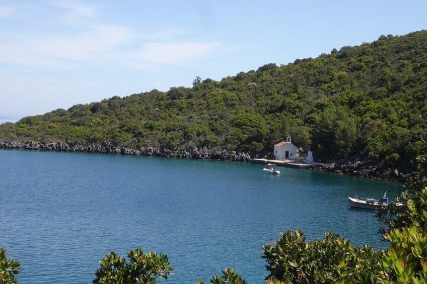 A coastal landscape with a small white building on a rocky shore, surrounded by calm blue waters and lush greenery. 2