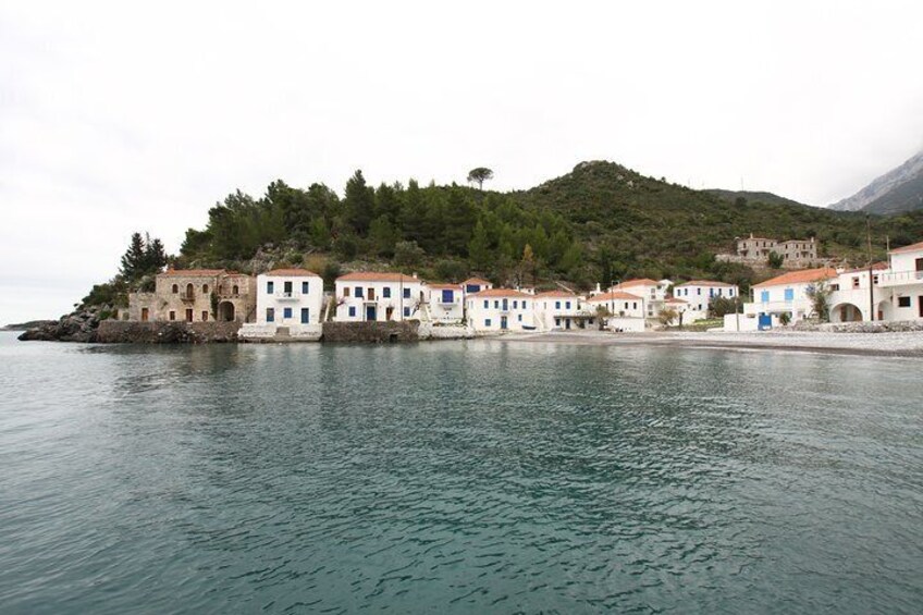 A coastal village with buildings along the shoreline, a hill with trees, and calm water. 3