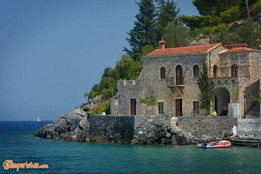 A stone building with a red roof by the sea, a small boat, and a sailboat in the distance. 3