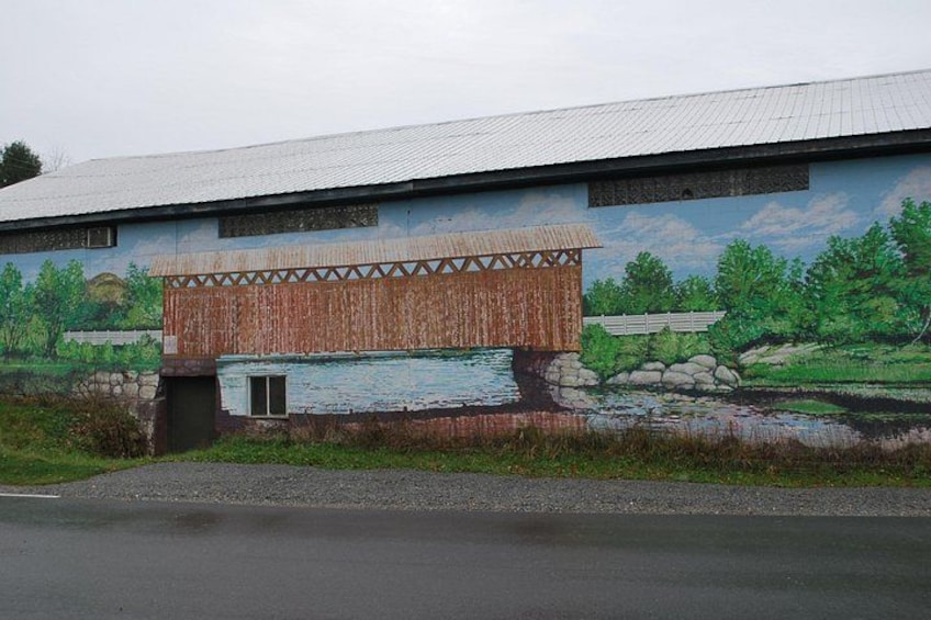 Un edificio con un mural que muestra un puente de madera y un río. 4