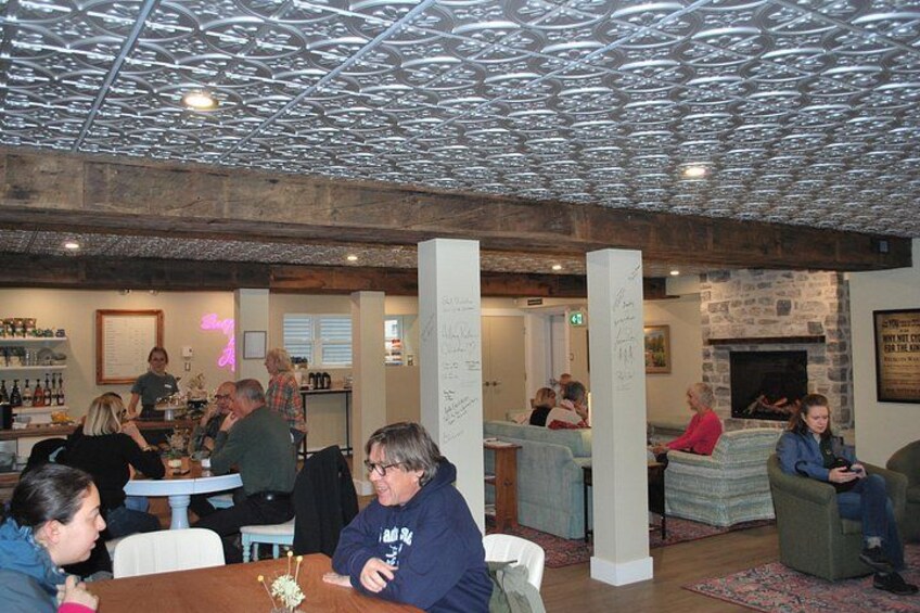 Un ambiente interior acogedor con vigas de madera, una zona de bar y gente sentada en mesas. 3