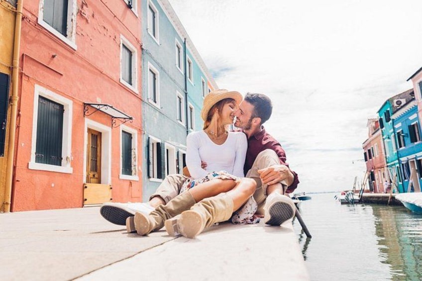 A couple sitting on a dock by a canal with colorful buildings in the background. 4