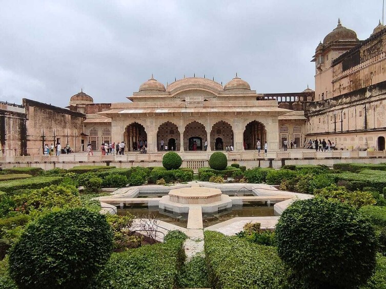 Un bâtiment historique doté de coupoles et d’arcades, entouré d’un jardin à la française avec une fontaine centrale. 3