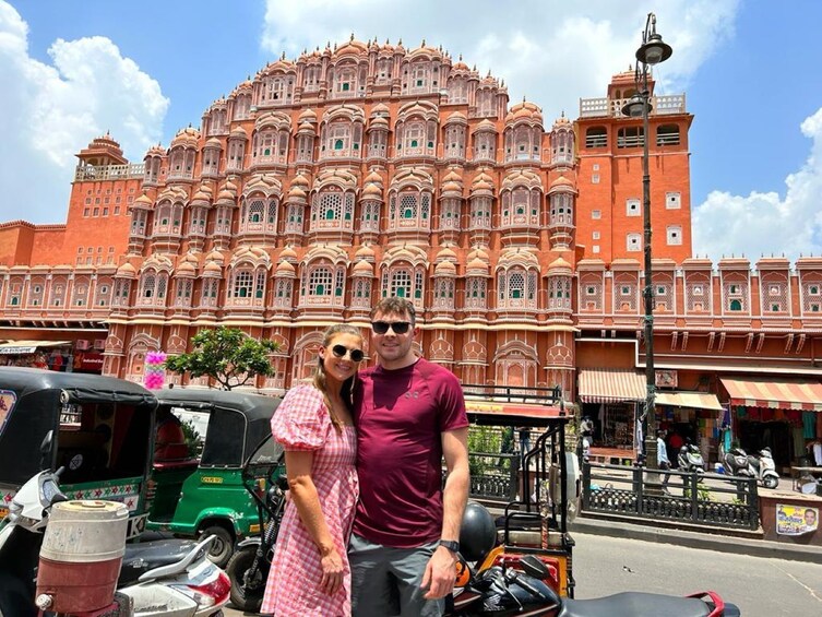 Un couple pose devant un grand bâtiment orné, dont l’architecture est riche en détails. 2