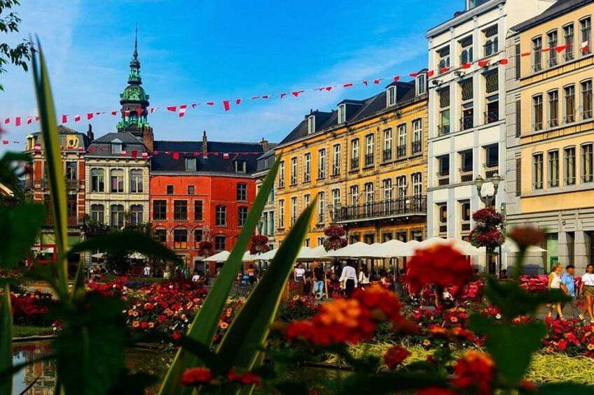 A European town square with colorful buildings, a prominent tower, and a flower-filled garden. 5