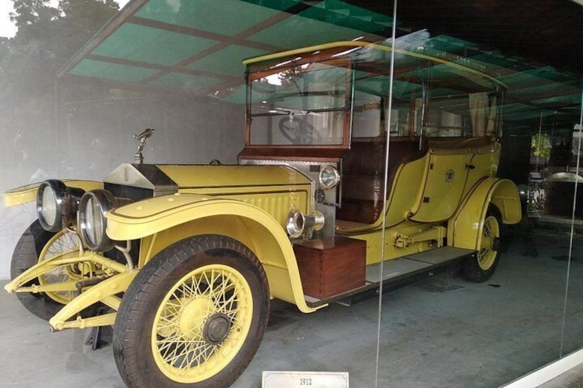 A yellow vintage car with a wooden dashboard and wire-spoke wheels, displayed in a glass case. 2