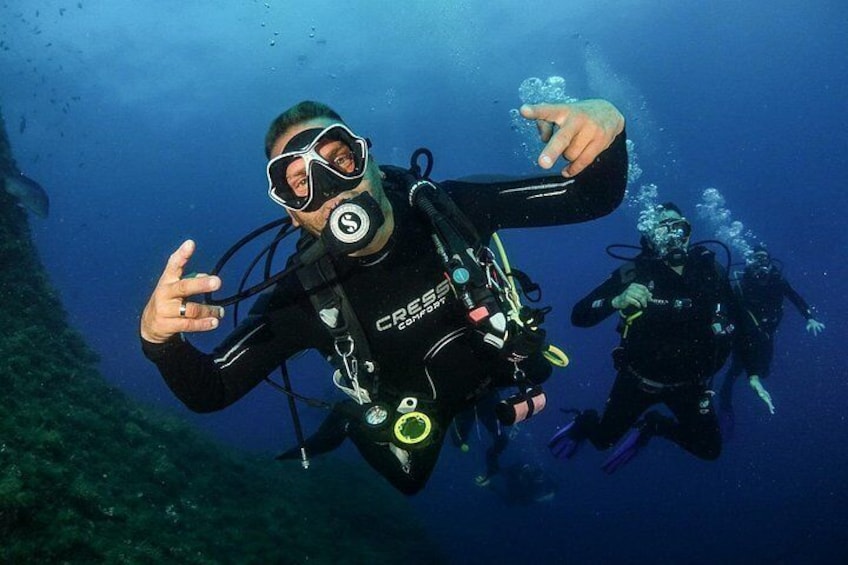 Two scuba divers underwater with scuba gear, one pointing towards the camera. 5