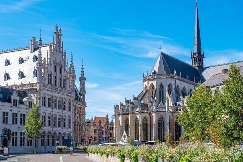 Een historisch Europees stadsplein met versierde gebouwen, waaronder een kerk met een hoge toren. 3