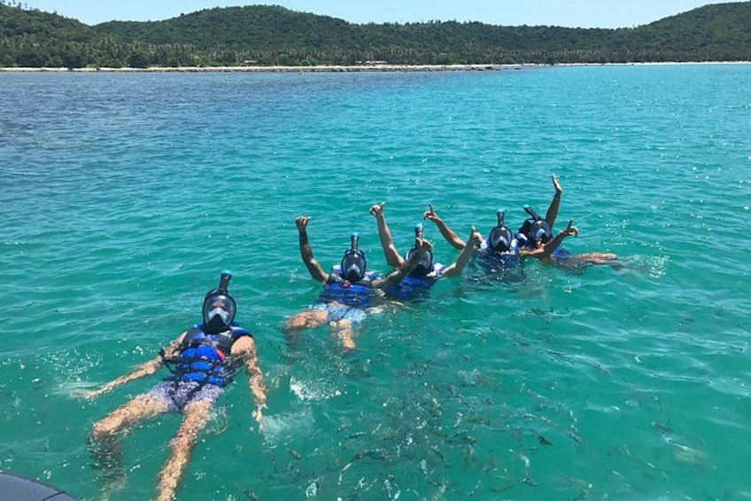 Personas haciendo snorkel en aguas azules cristalinas, con un paisaje montañoso al fondo. 1