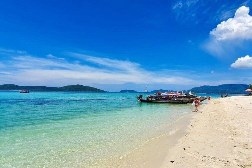 Una playa con agua turquesa cristalina, un bote en la orilla y montañas distantes. 2
