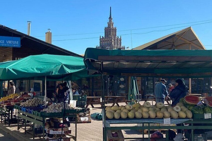 Ein Markt im Freien mit Gemüseständen und einem historischen Gebäude im Hintergrund. 3