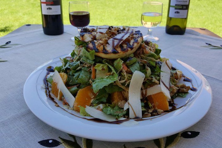 Een bord eten met salade, gegrild vlees en groenten op een tafel met wijnflessen en glazen. 3