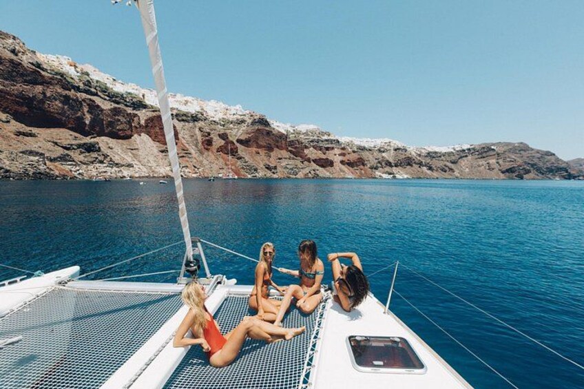 Un velero con gente relajándose en la cubierta, rodeado de aguas azules tranquilas y acantilados rocosos. 2