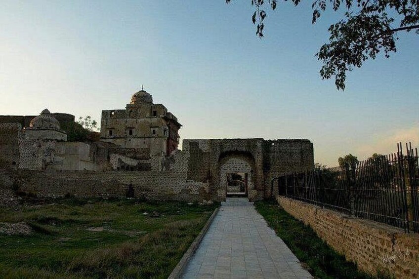 An ancient stone structure with a dome and arched entrance, surrounded by a low stone wall and a metal fence. 3