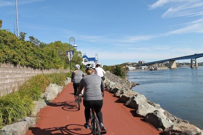 Un groupe de cyclistes sur une piste rouge au bord d’une rivière, avec un pont en arrière-plan. 1