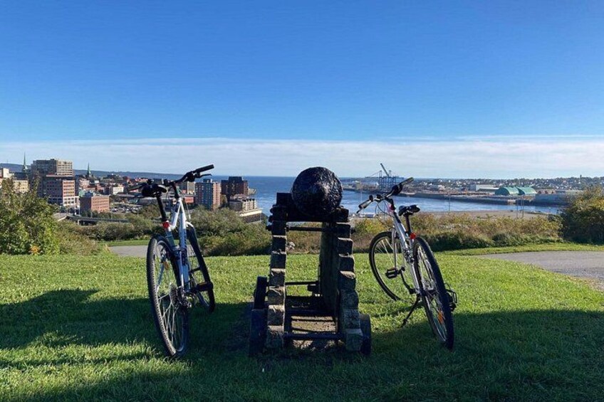 Un espace verdoyant avec deux vélos garés, une structure en pierre et, en arrière-plan, une vue sur la ville. 2