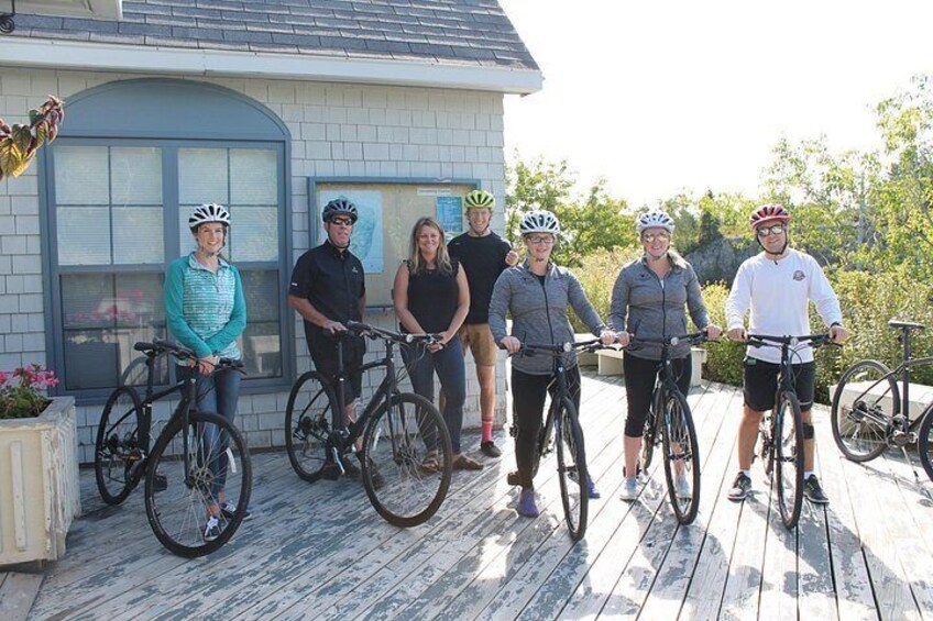 Un groupe de personnes se trouve sur une terrasse en bois, avec des vélos, une maison et de la verdure en arrière-plan. 5