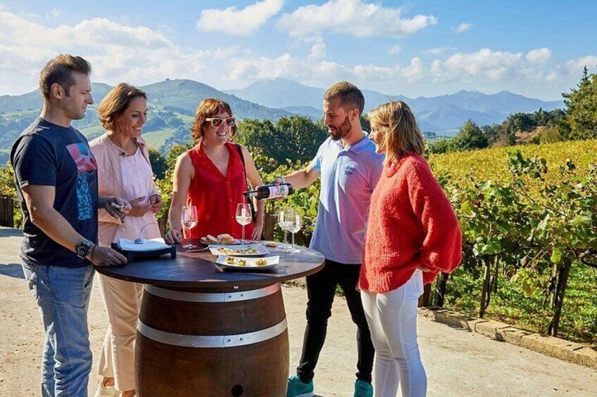 Un grupo de personas de pie alrededor de un barril, con un viñedo y montañas al fondo. 5