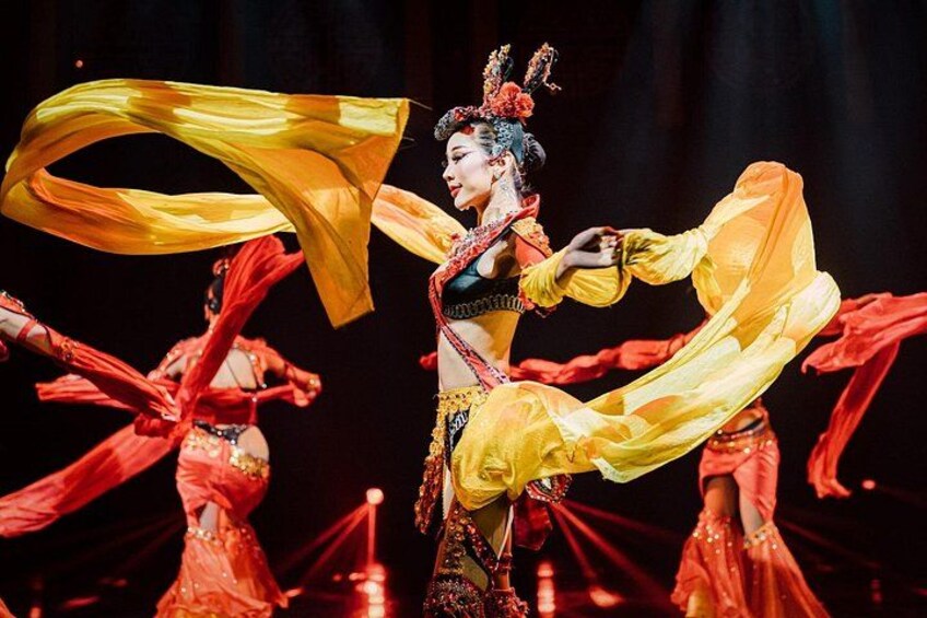 A performer in traditional costume with flowing yellow and red fabric, performing on stage. 2