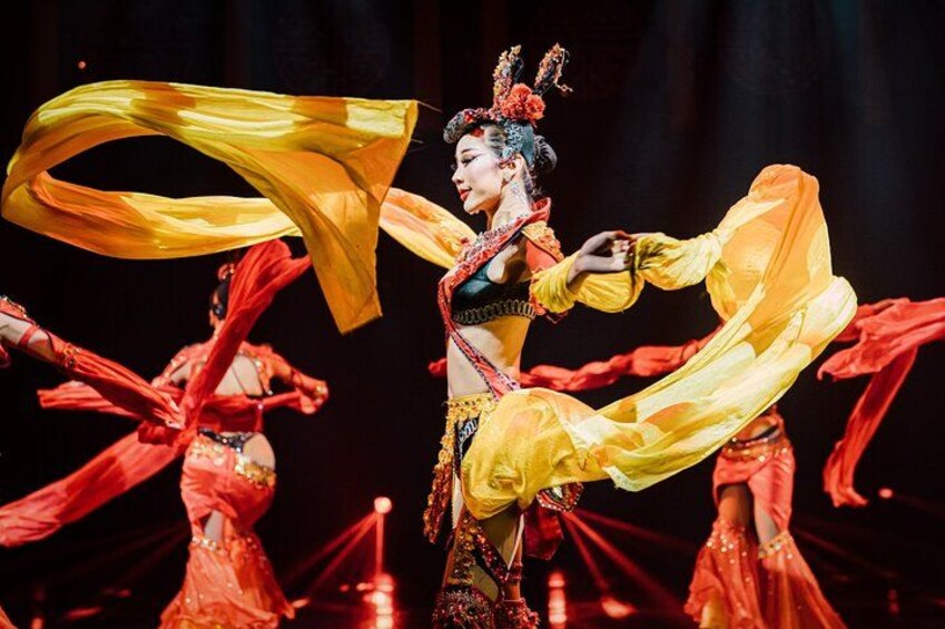 A performer in a yellow costume with flowing fabric, surrounded by others in red costumes. 2