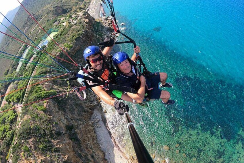 To personer paraglider over en kystklint med klart, blåt vand nedenfor. 1