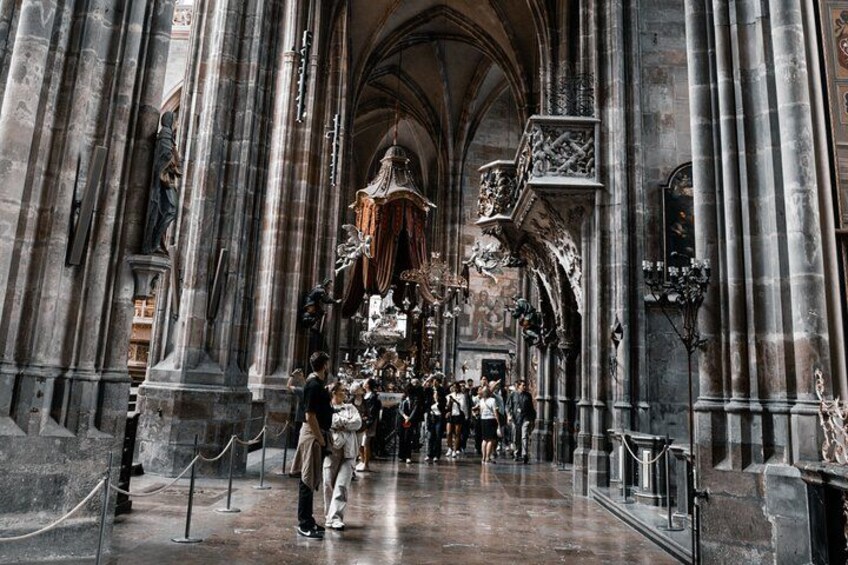 Ein gotischer Kirchenraum mit hohen Gewölben, großen Steinsäulen und einem zentralen Altar mit religiösen Figuren. 2