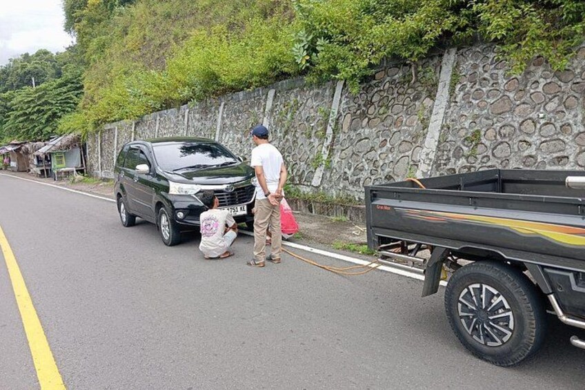 A road with a green car, a man, and a woman near a stone wall. 3