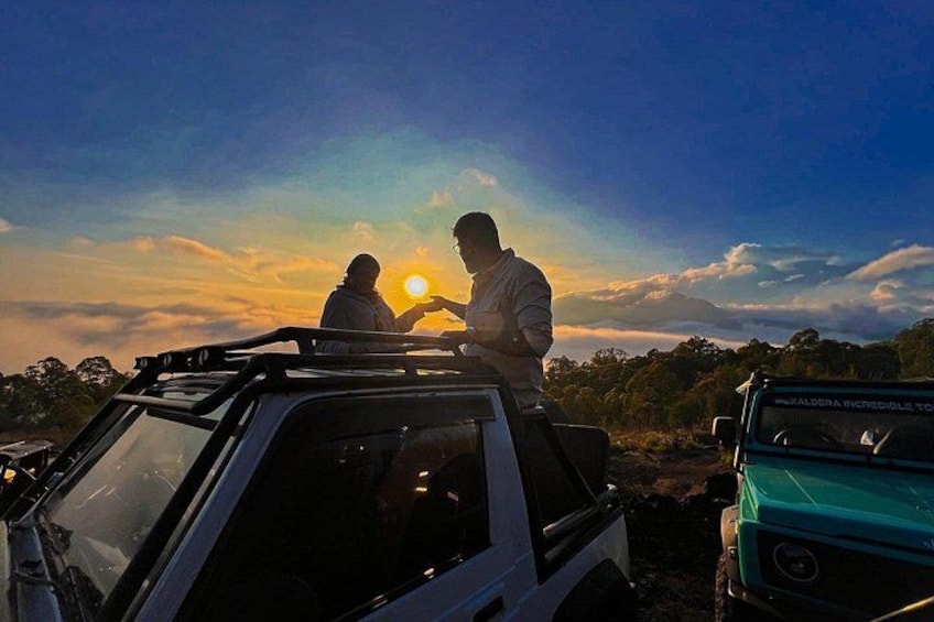 Two people standing on a vehicle with a sunset in the background. 2