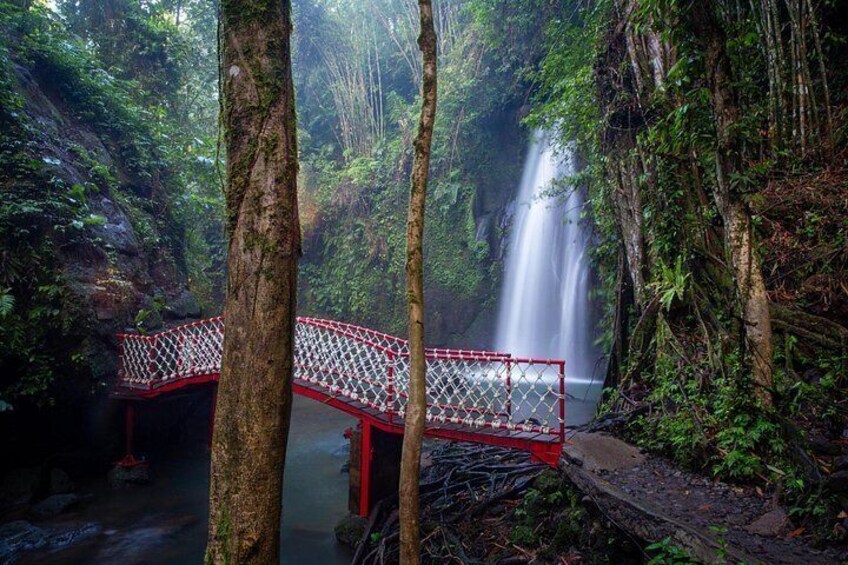 A red bridge over a river in a forested area with a waterfall in the background. 3