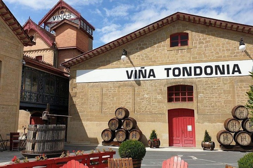 A building with a sign that reads 'VIÑA TONDONIA' and several wine barrels outside. 1