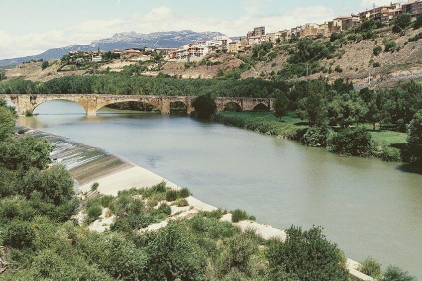 A river with a bridge, greenery, and buildings on a hillside. 3