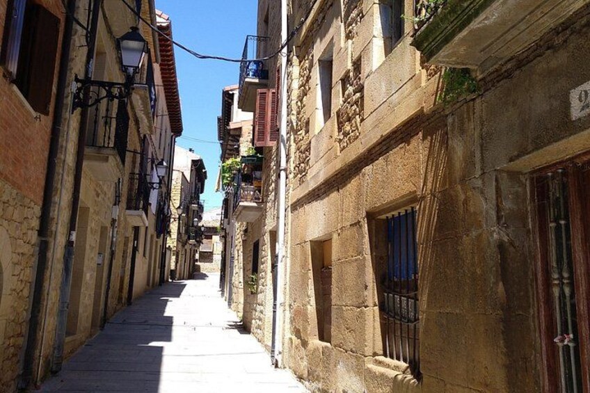 A narrow street flanked by historic stone buildings with balconies and shutters. 2
