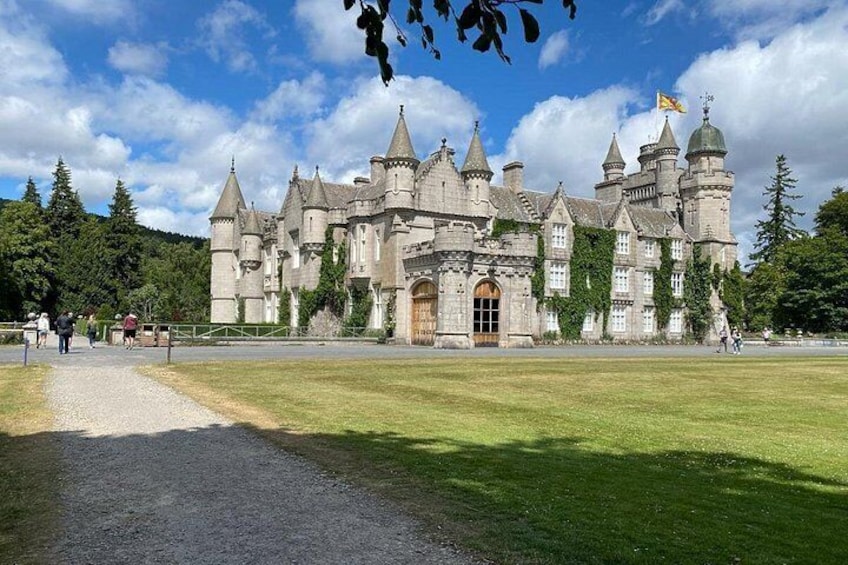 A historic castle with multiple towers and turrets, surrounded by a well-maintained lawn and a gravel path leading to the entrance. 4