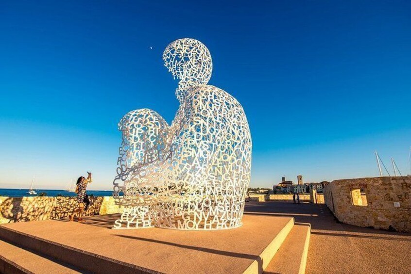 A large, intricate metal sculpture of a seated figure on a beach. 1