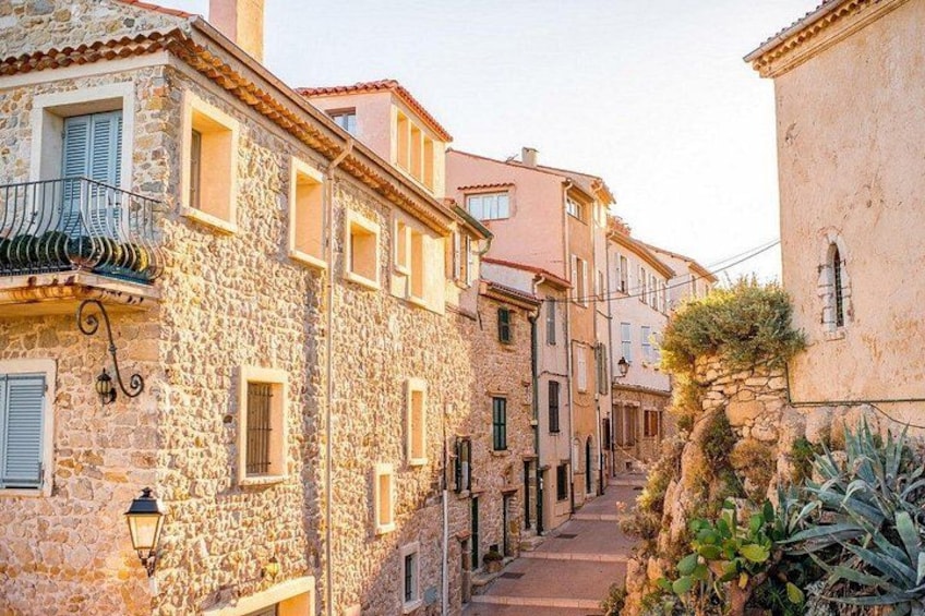 A narrow stone street flanked by old buildings with balconies and shutters. 5
