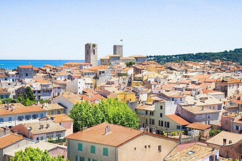 A coastal town with historic buildings, a prominent tower, and a clear view of the sea. 2