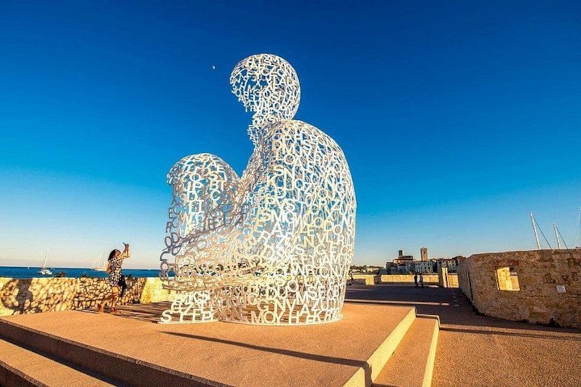 A large metallic sculpture of a seated figure on a beach. 3