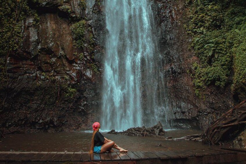 A waterfall, a person sitting on a wooden platform, and a rocky cliff. 3