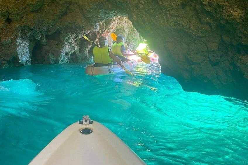 A kayak navigating through a turquoise water body with a rocky cave entrance in the background. 2