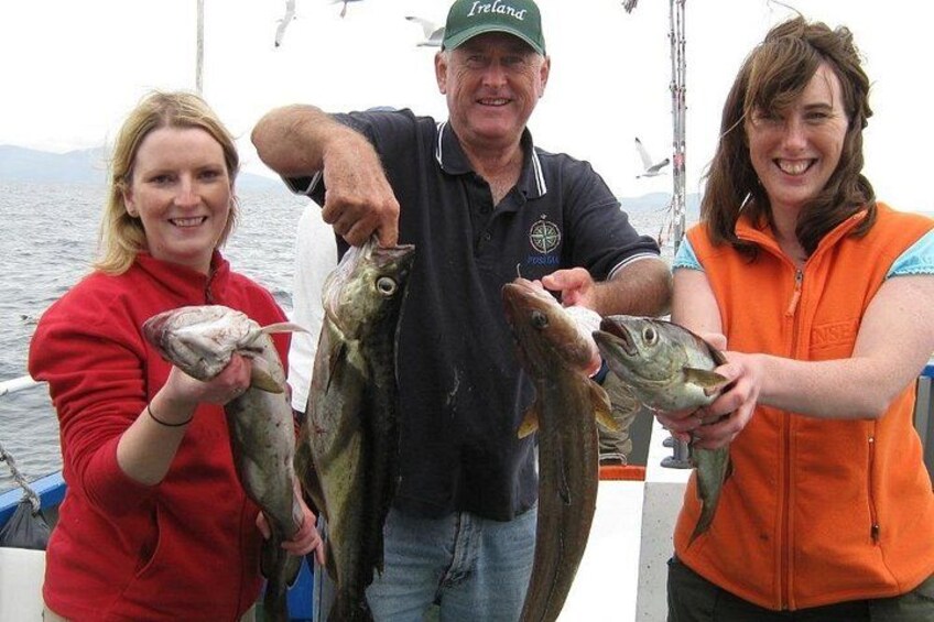 Three people holding fish on a boat with a body of water and mountains in the background. 1