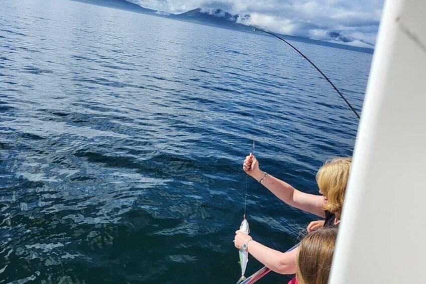 A person fishing on a boat with a clear view of the ocean and distant mountains. 2