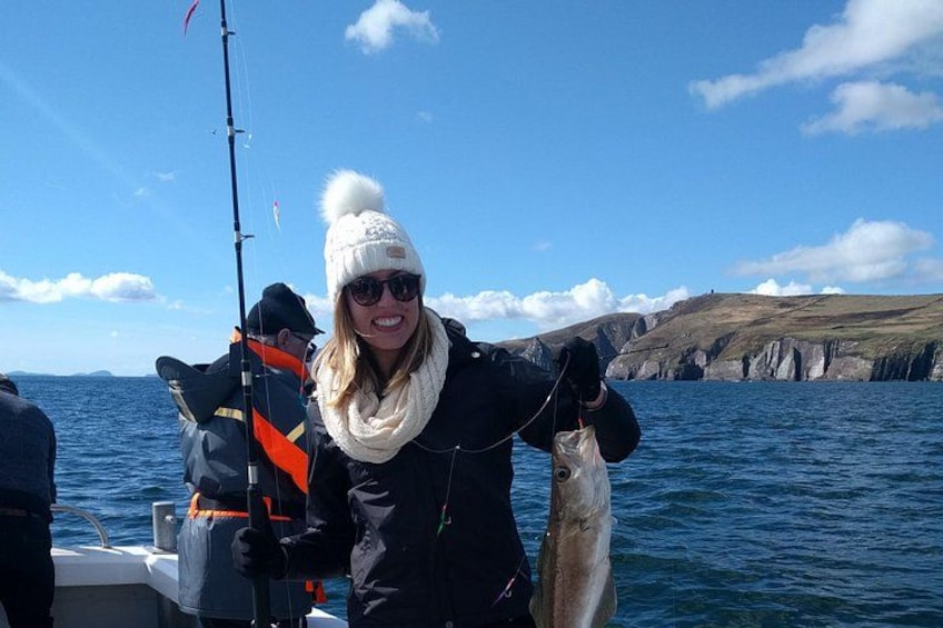 A person holding a fish on a boat with a rocky coastline in the background. 5