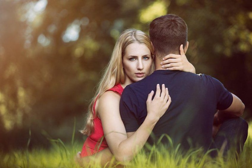 A couple embracing in a grassy area with trees in the background. 1