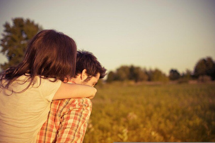 Two people embracing in a field with trees in the background. 3