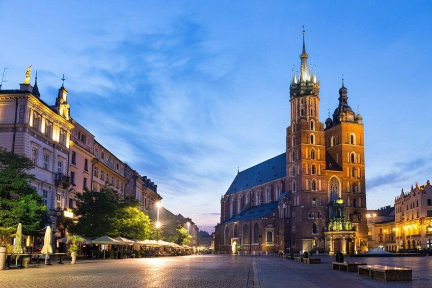 A historic building with a prominent tower, a wide street, and surrounding trees. 1