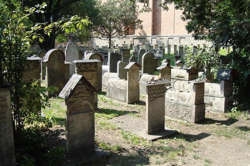 A cemetery with numerous headstones, some with inscriptions, surrounded by trees and greenery. 2