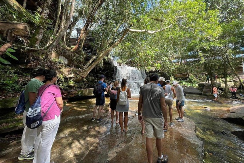 A waterfall in a forested area with people observing it. 2