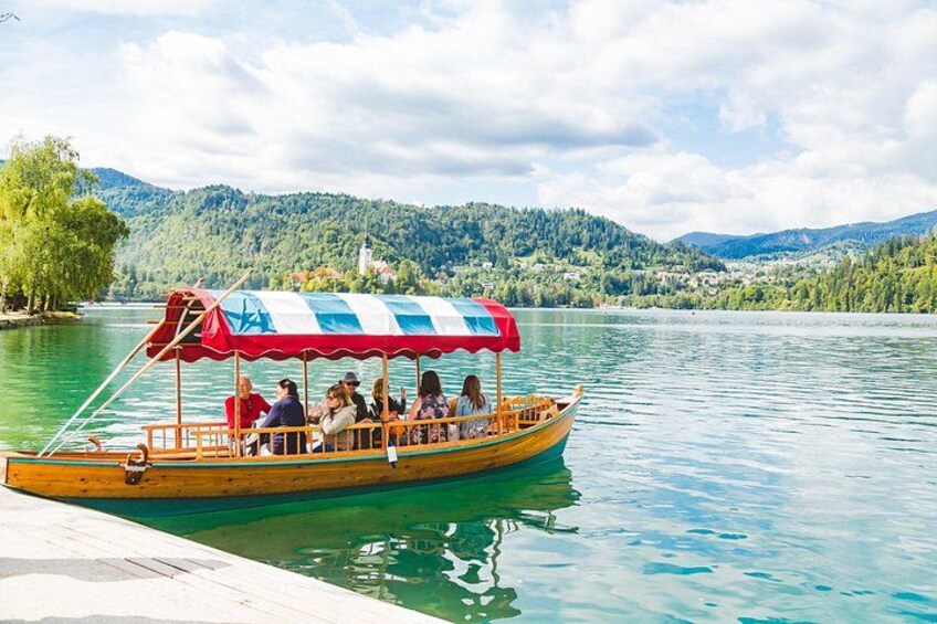 Un bote de madera con pasajeros, un toldo a rayas azul y rojo, y un lago con montañas al fondo. 5